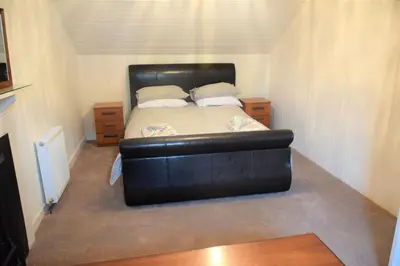 a bed in a small room with a black leather couch at Coachmans Cottage in Carsethorn