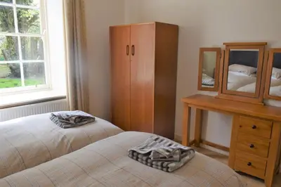 a bedroom with two beds and a dresser and a mirror at Coachmans Cottage in Carsethorn