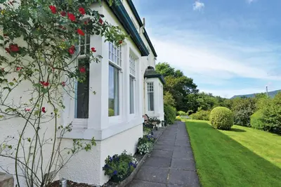 a white house with red flowers on the side of it at Skiddaw Grove in Keswick