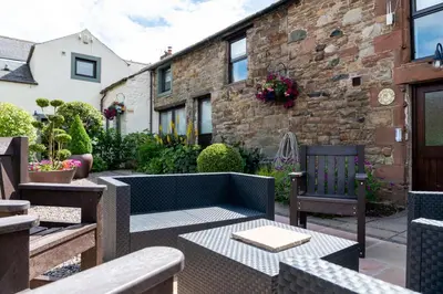 a patio with a couch and chairs and a building at Brae Fell Cottage, Sebergham, Nr Caldbeck dog friendly and hot tub in Sebergham