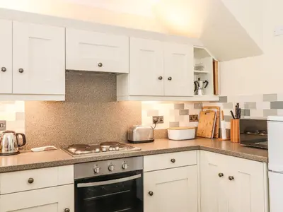 a kitchen with white cabinets and a stove top oven at Primrose Cottage in Keswick