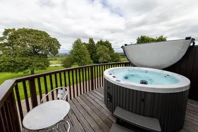 a hot tub on a deck with a table and a chair at Cloven Stone, Nr Caldbeck ideal family accommodation with hot tub in Sebergham