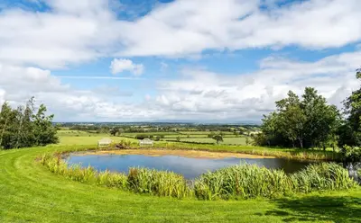 a pond in the middle of a green field at Fisher Gill, Sebergham, Close to Caldbeck Fells with hot tub in Sebergham