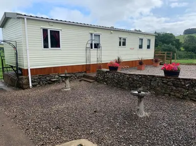 a small white house with a stone wall at Farm stay caravan on working farm in Dacre