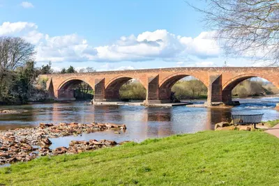 a bridge over a river with dogs in the water at Cottage - Sleeps 3 hot tub & pet friendly in Carlisle