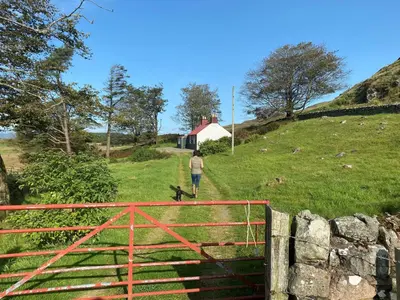 a person walking a dog on a field with a fence at The Drovers Cabin in Kirkcudbright
