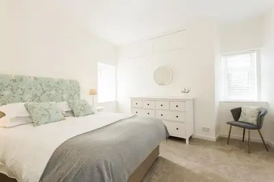 a white bedroom with a bed and a chair at 118 High Street in Kirkcudbright