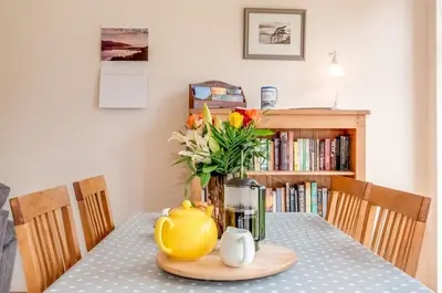 a dining room table with a yellow tea pot and flowers at Kinnen Cottage in Creetown