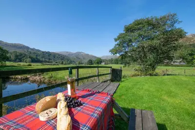 a picnic table with a view of a river and mountains at 2 Bed in Grasmere oc-gl081 in Grasmere