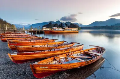 a row of wooden boats sitting on the shore of a lake at 2 Bed in Portinscale oc-gl129 in Portinscale