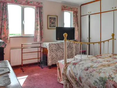 a bedroom with a bed and a table and windows at Rose Rigg Cottage in Kirklinton