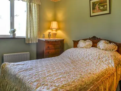 a bedroom with a bed and a lamp and a window at Rose Rigg Cottage in Kirklinton