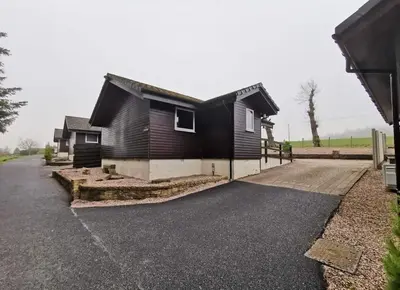 a house with a black roof on a driveway at Cairnyard Lodges - Woodside in Beeswing
