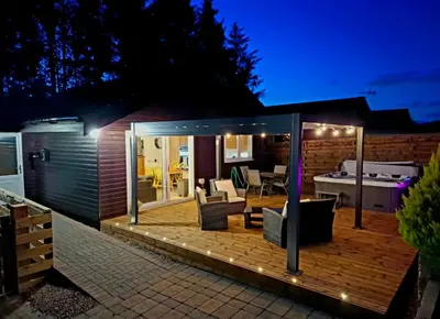 a deck with a hot tub in a house at night at Cairnyard Lodges - Woodside in Beeswing
