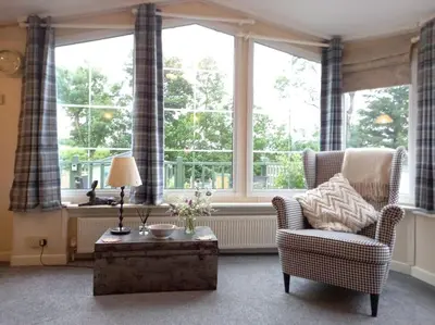 a living room with a chair and a table and windows at Treetops in Lamplugh