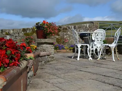 a patio with white chairs and a table and flowers at Rosedale- Lyl in Ireby
