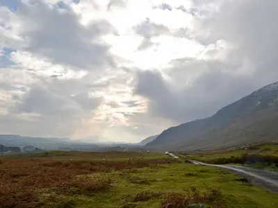 a winding road in the mountains under a cloudy sky at Swaledale Cottag in Caldbeck