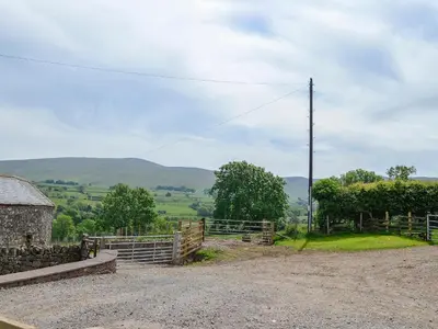 a dirt road with a fence and a barn at Swaledale Cottag in Caldbeck