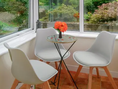 four white chairs and a table with a vase of orange flowers at Briar Bank Bungalow in Cockermouth