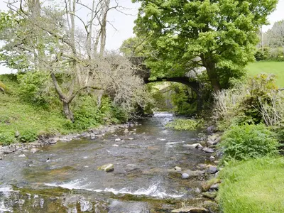 a river with a bridge in the background at The Corn Mill in Branthwaite