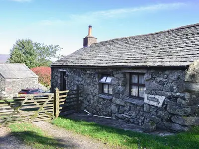 an old stone house with a wooden fence in front of it at Birkerthwaire Stable-W41477 in Eskdale