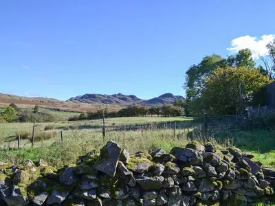 a stone wall in a field with mountains in the background at Birkerthwaire Stable-W41477 in Eskdale