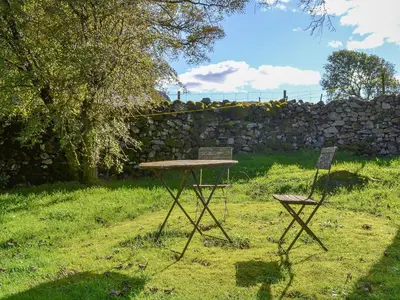 a picnic table and two chairs in a yard with a stone wall at Birkerthwaite Barn-W41478 in Eskdale