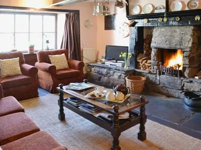 a living room with a fireplace and a table at Birkerthwaite Farmhouse in Eskdale