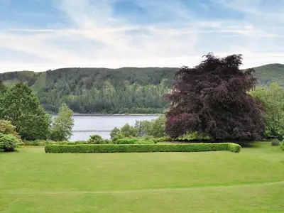 a green yard with a large tree and a lake at Grooms Room in Thirlmere