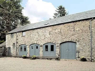 a brick building with three garage doors and trees at Aira Cottage in Watermillock