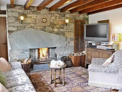 a living room with a stone fireplace and a tv at Whistling Green in Ulpha
