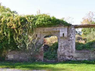 an old stone wall with an arch in the grass at Whitehall Pele Tower in Mealsgate