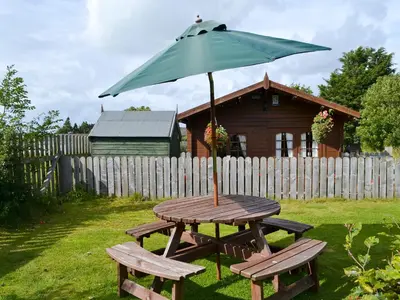 a picnic table with an umbrella and two benches at Hedgehog Meadows in Waverton