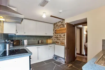 a kitchen with white cabinets and a stone wall at The Coppermines Mountain Cottages - Carpenters, Millrace, Pelton Wheel, Sleeps 14 in Coniston