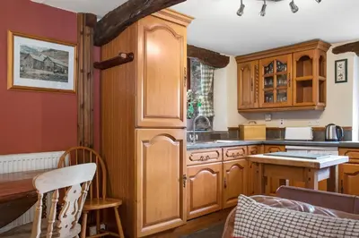 a kitchen with wooden cabinets and a table at The Coppermines Mountain Cottages - Sawyers, Carpenters, Pelton Wheel, Sleeps 18 in Coniston