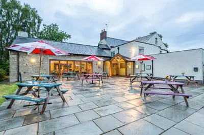 a patio with picnic tables and umbrellas in front of a building at The Queens in Carlisle
