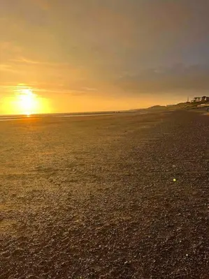 a beach with the sun setting in the distance at Lake District Coastal cottage in Seascale