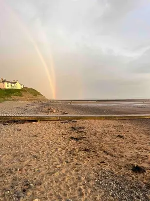 a rainbow over the beach with a house in the background at Lake District Coastal cottage in Seascale