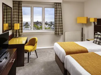 a hotel room with two beds and a desk and window at Mercure Ayr Hotel in Ayr