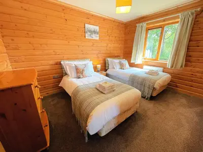 two beds in a room with wooden walls at Beautiful 2BR Beach Lodge Set In Stunning Gardens - Pass the Keys in Dalbeattie