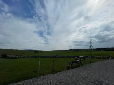 a bench in a field with a cloudy sky at Lake District Luxury Lodge in Plumbland