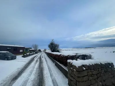 a road covered in snow with a stone wall at Lake District Luxury Lodge in Plumbland