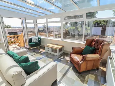 a conservatory with a couch and chairs in a room with windows at Rose Bank Cottage in Carlisle