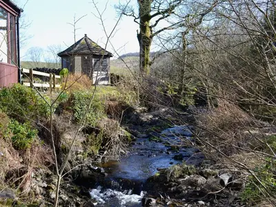 a stream with a small building next to a river at Arkland Mill in Corsock