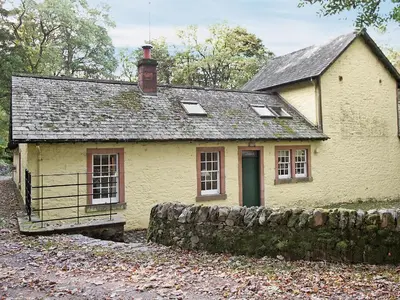 an old yellow house with a stone wall at Stables Cottage-Uud in Corsock