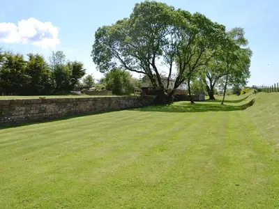a large field with a tree and a wall at The Carriage in Bridge of Dee