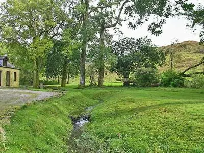 a stream in a field next to a house at Marwhin Cottage - Swws in Kirkpatrick Durham