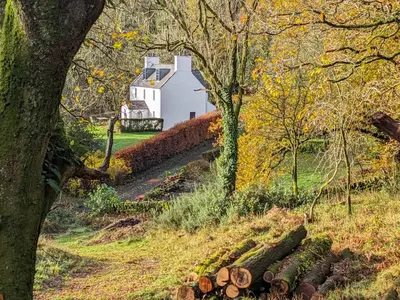 a white barn in the middle of a field with trees at Little Boreland in Gatehouse of Fleet