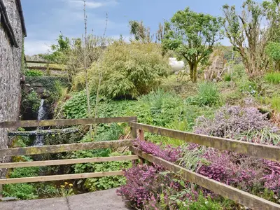 a wooden fence next to a garden with a waterfall at The Hen Hoose in Creebridge