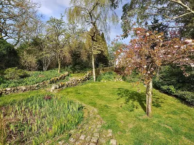 a garden with a stone wall and a tree at Holly Cottage - 28140 in Boreland of Colvend